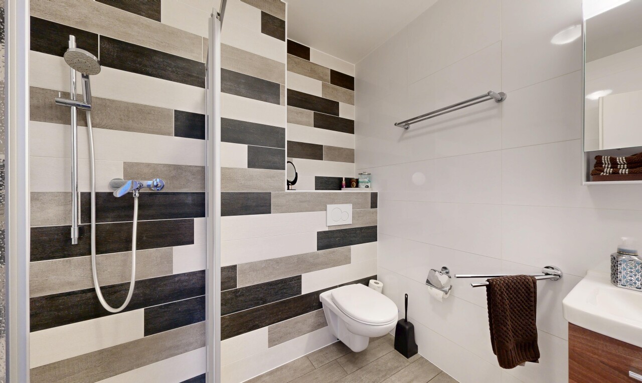 salle de bains avec salle de bain complète, douche, miroir, lavabo (ou coiffeuse selon le contexte), et mur en carrelage