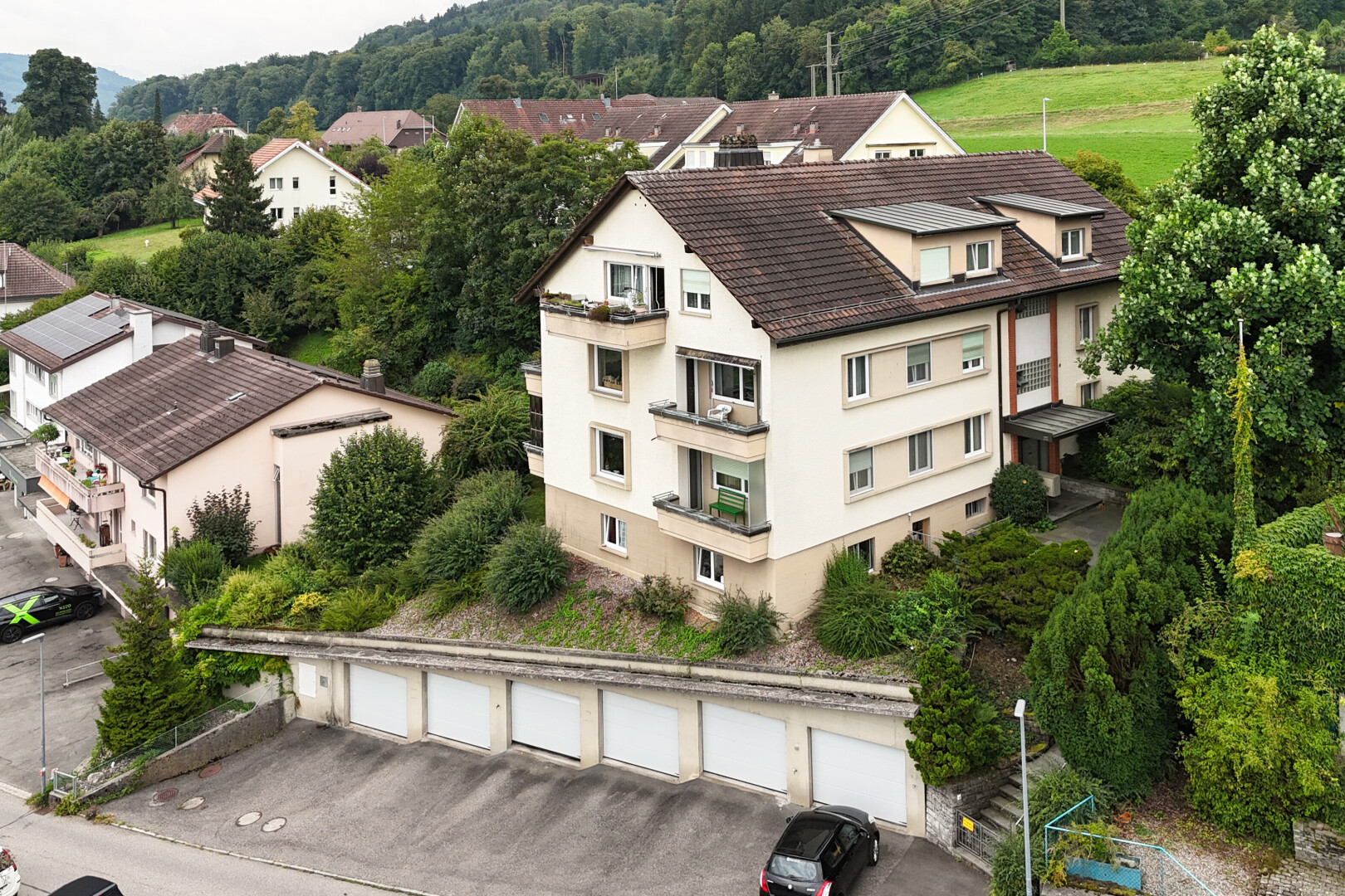 façade avec bardage en stuc, toit mansardé, garages communautaires, et drone view