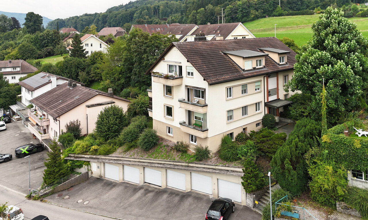 façade avec bardage en stuc, toit mansardé, garages communautaires, et drone view