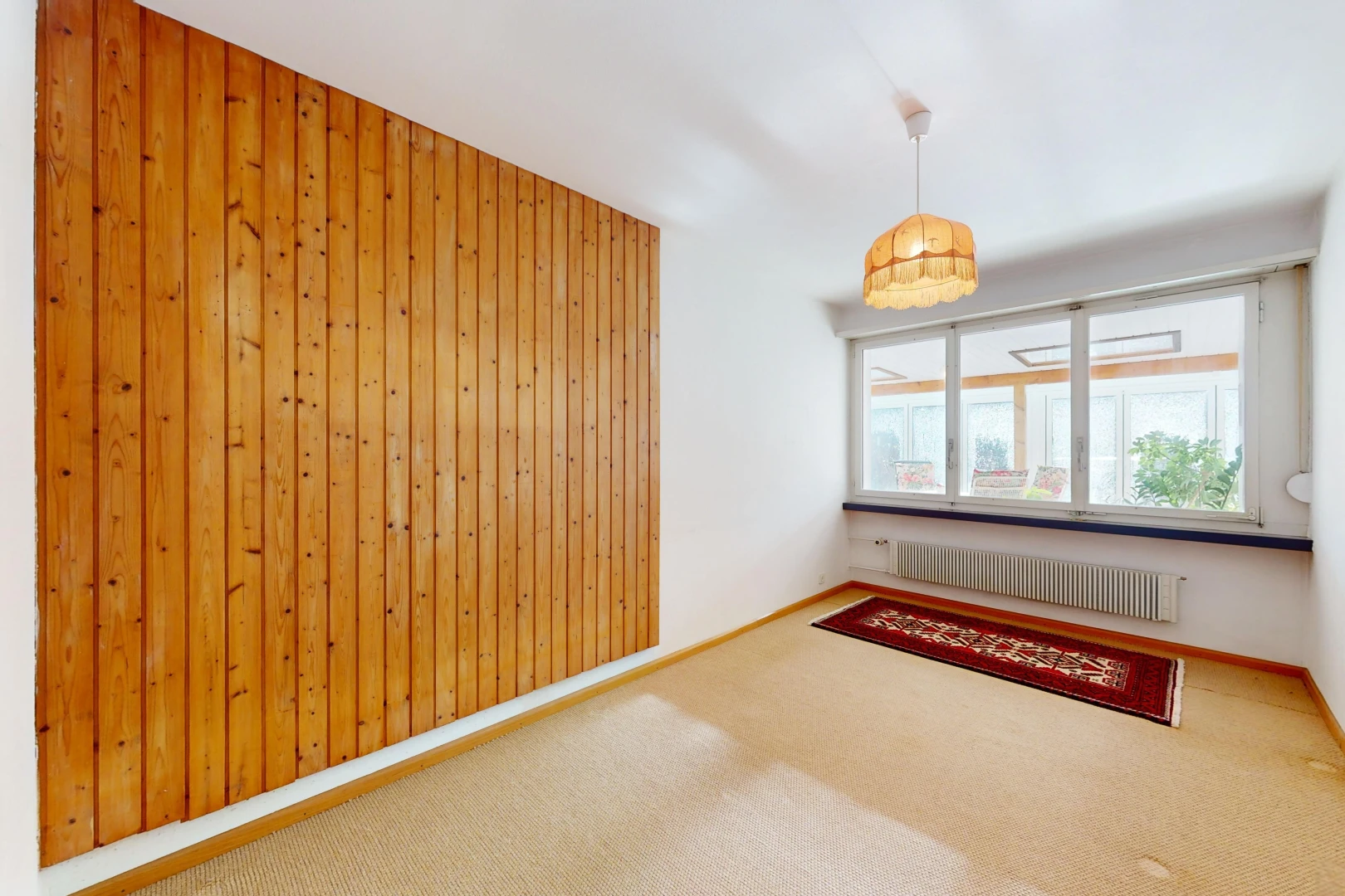 pièce vide avec radiateur, mur en bois, moquette, et lumière naturelle