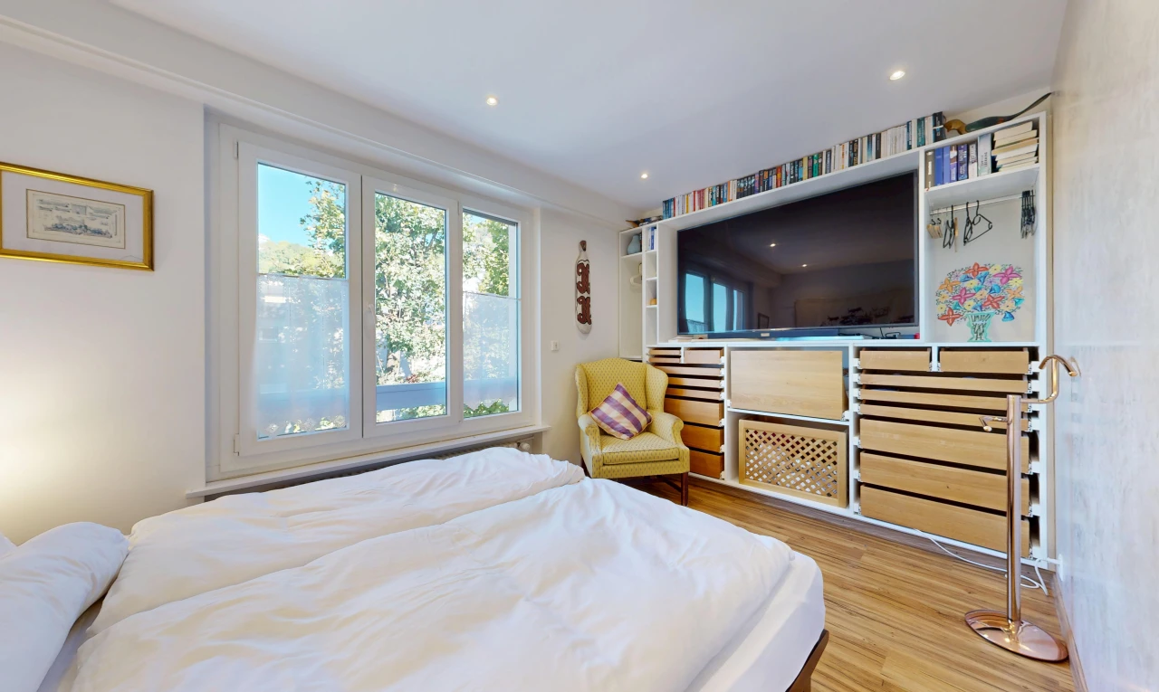 chambre avec télévision, étagères intégrées, sol en finition bois, wood finish floor, et éclairage encastré