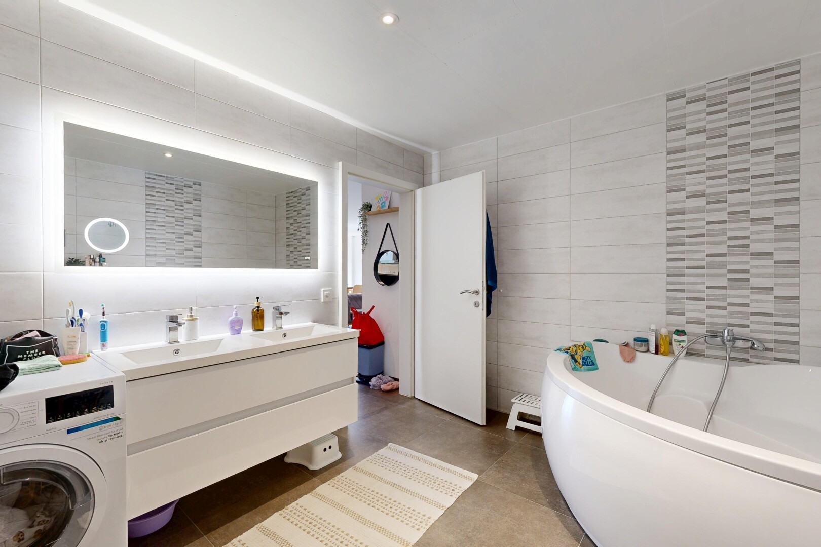 salle de bains avec mur en carrelage, tile wall, bain, double vasque, et lave-linge et sèche-linge