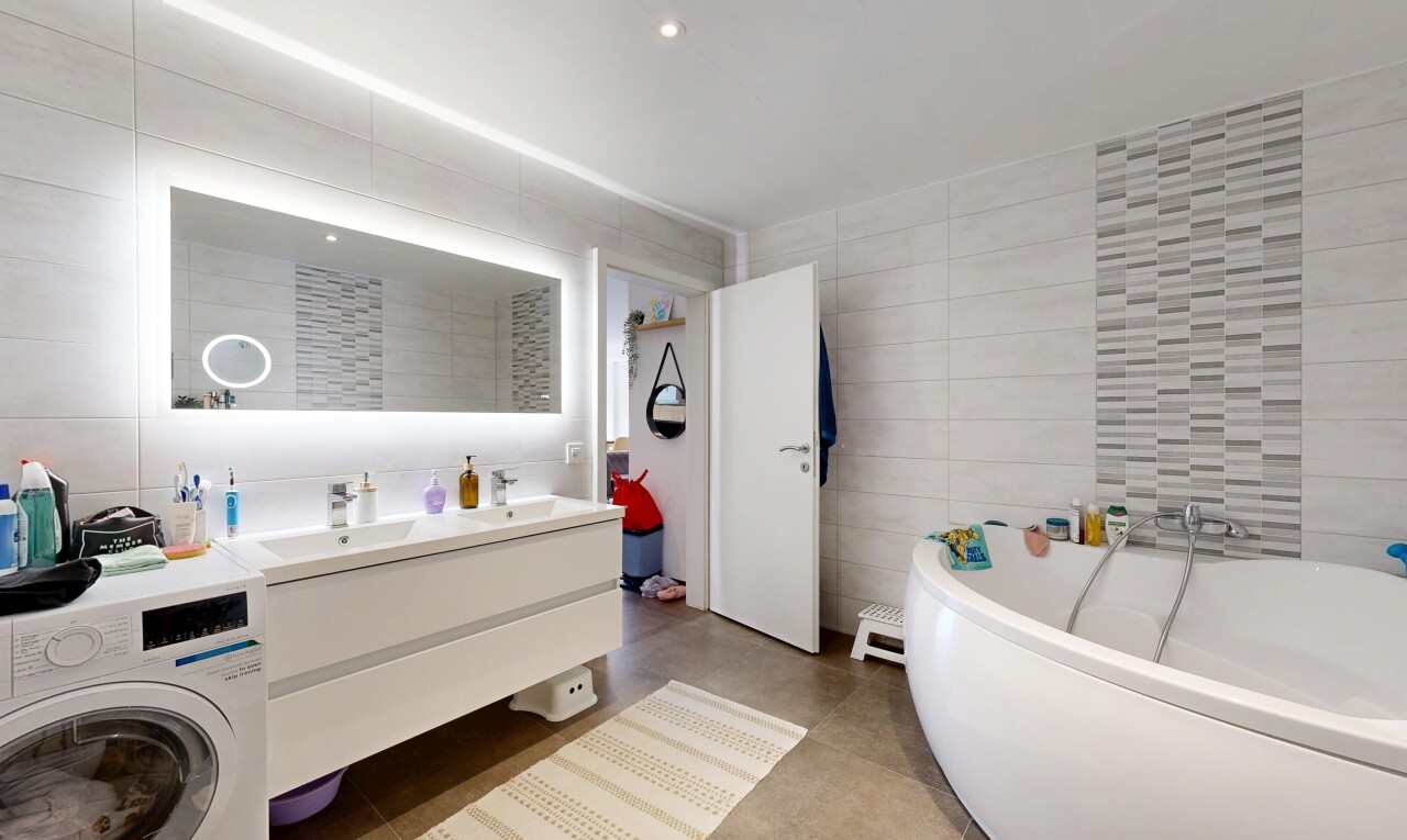 salle de bains avec mur en carrelage, tile wall, bain, double vasque, et lave-linge et sèche-linge
