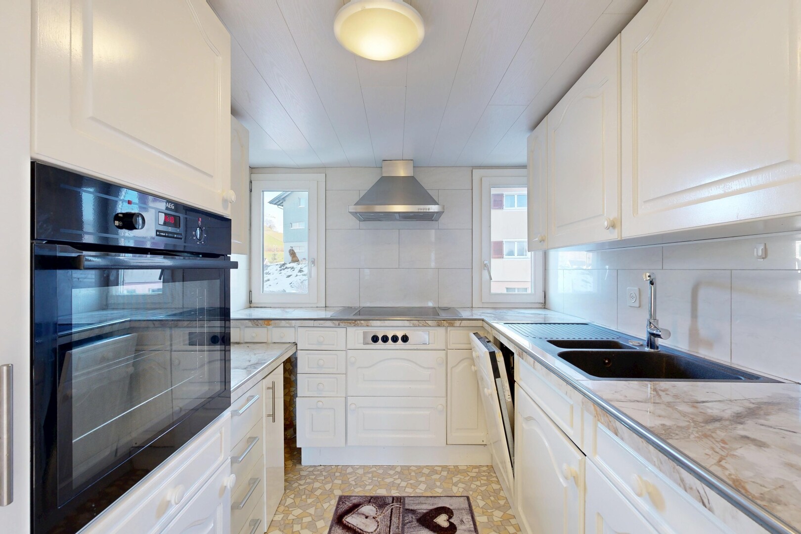 kitchen featuring black oven, white cabinetry, light countertops, and wall chimney range hood