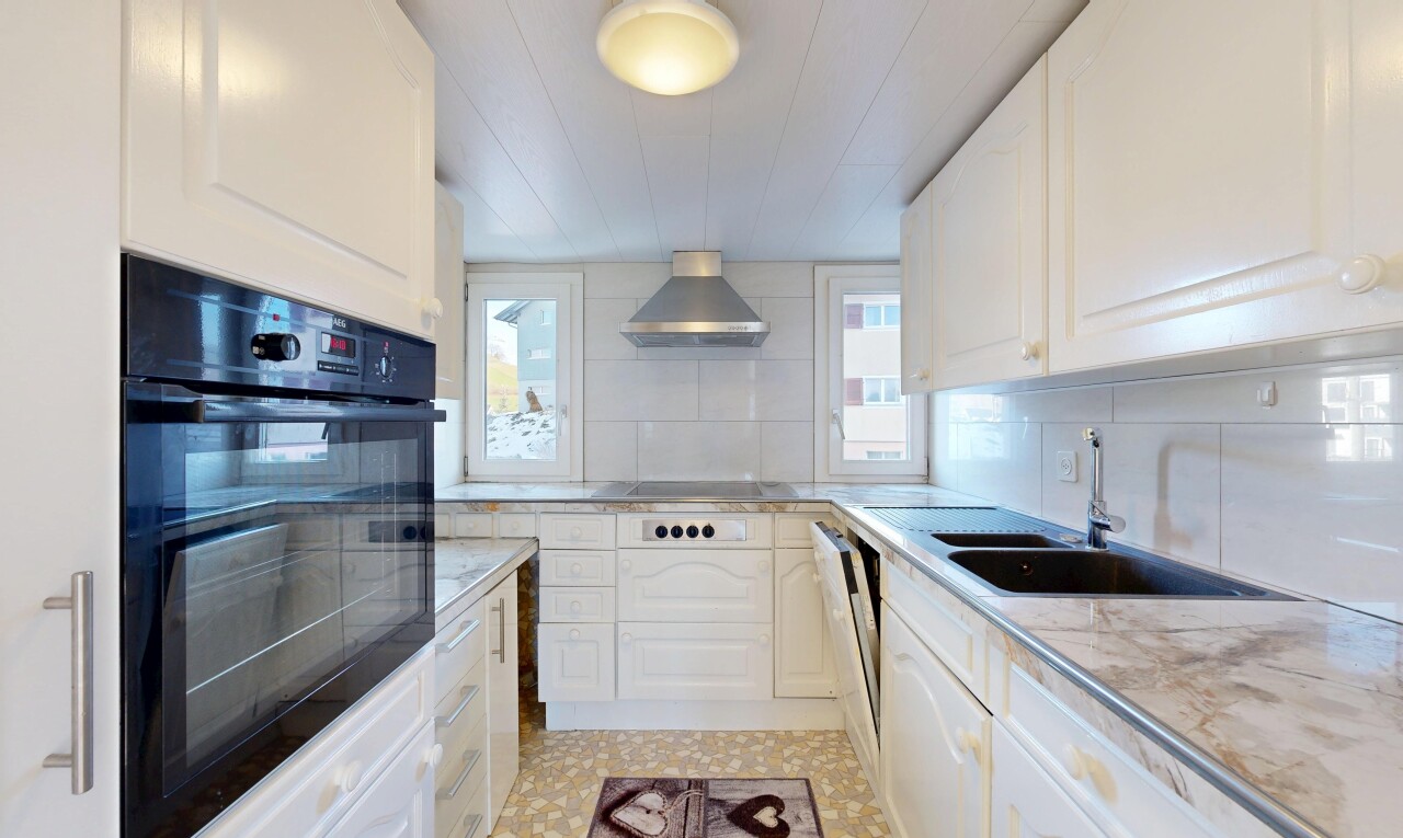 kitchen featuring black oven, white cabinetry, light countertops, and wall chimney range hood