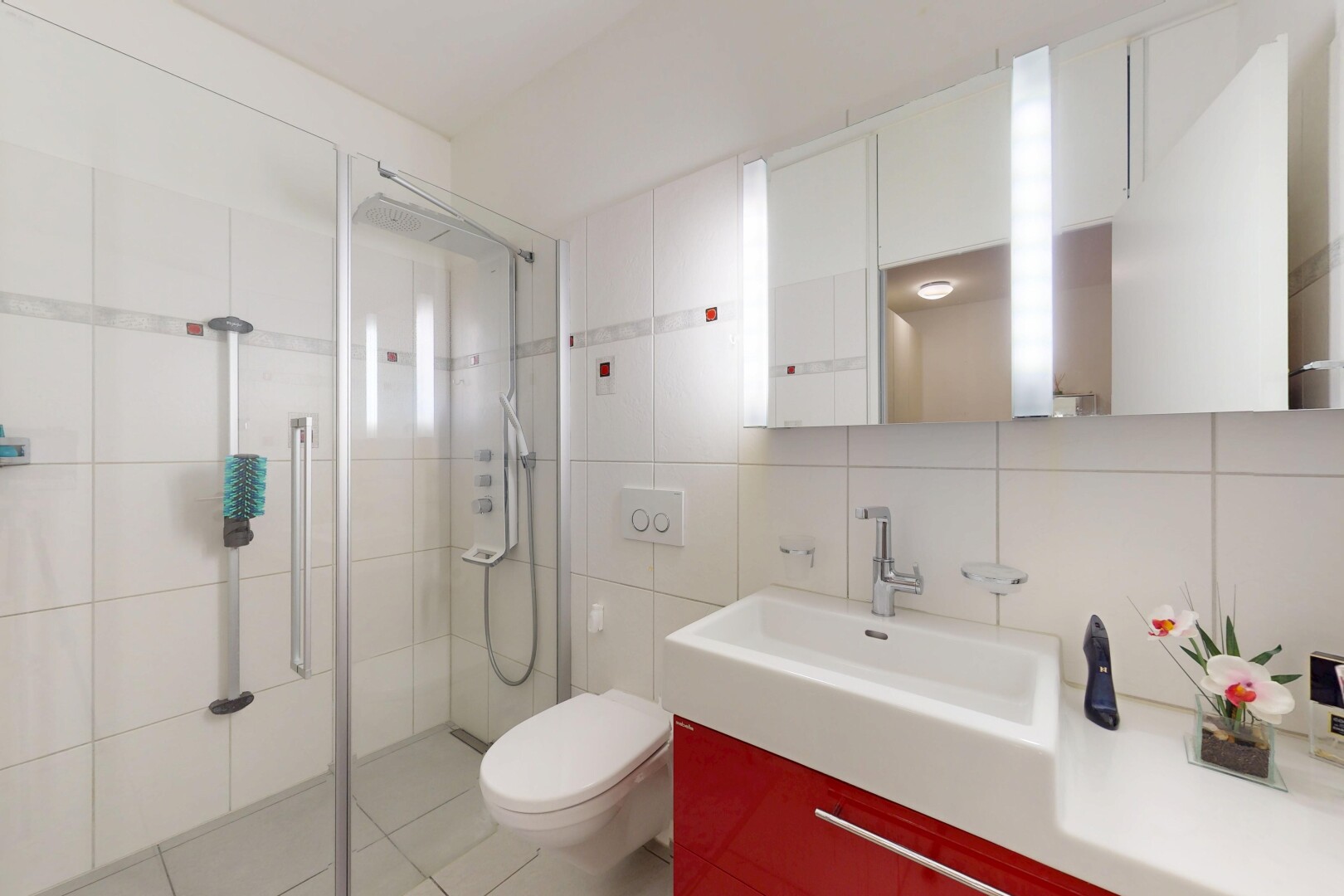 salle de bains avec toilette, douche, mur en carrelage, évier, et miroir