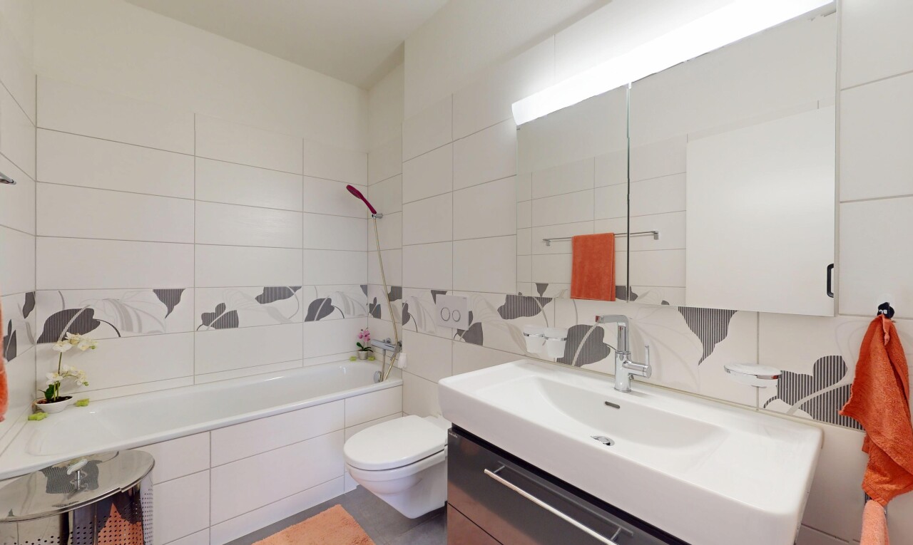salle de bains avec toilette, mur en carrelage, salle de bain complète, miroir, et lavabo (ou coiffeuse selon le contexte)
