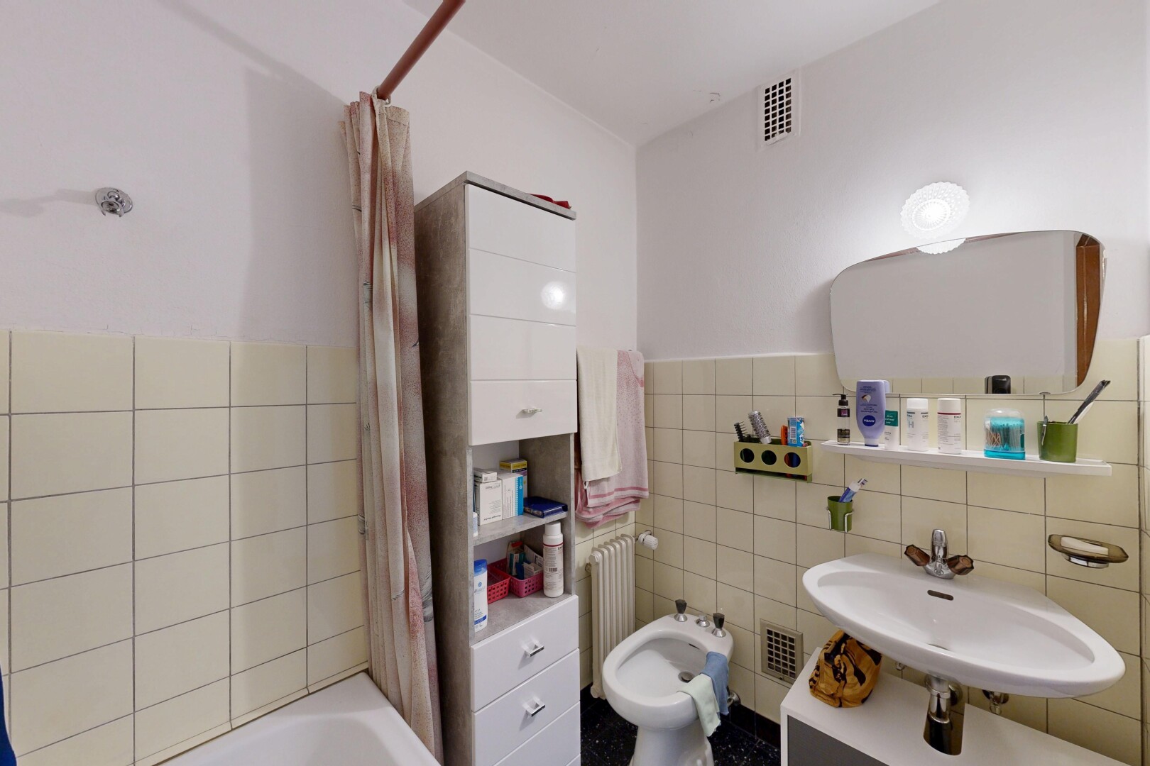 full bath featuring tile walls, a bidet, shower / bath combination with curtain, a wainscoted wall, and radiator
