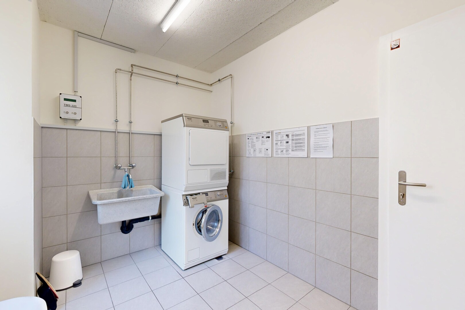 buanderie avec tile wall, lave-linge et sèche-linge superposés, drywall, inside community, et tile floor