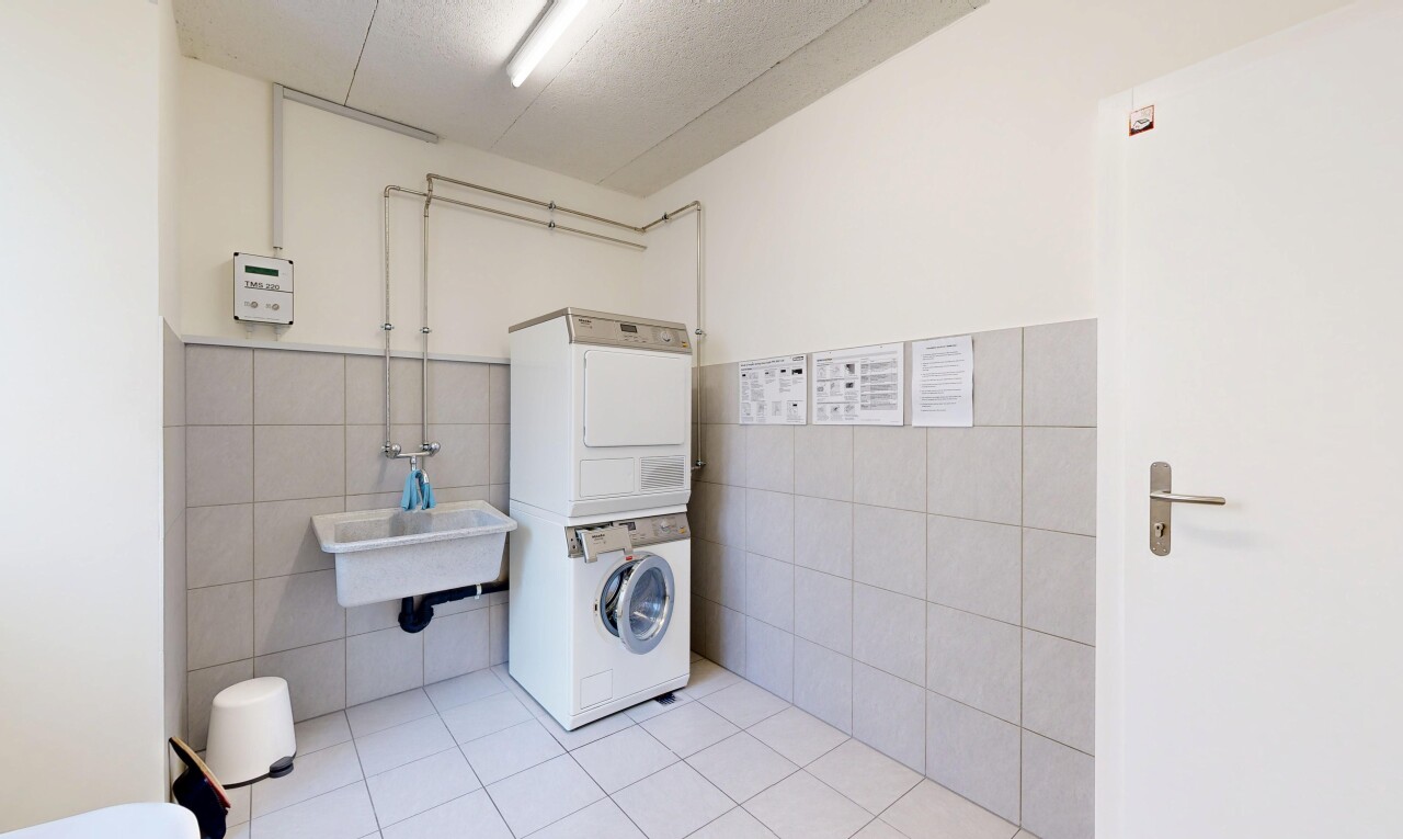 buanderie avec tile wall, lave-linge et sèche-linge superposés, drywall, inside community, et tile floor