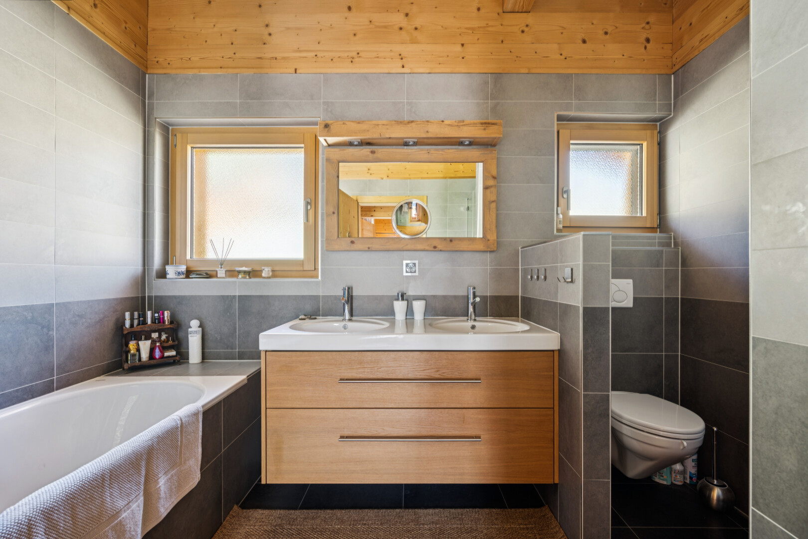full bath with tile walls, double vanity, a garden tub, and dark tile patterned floors