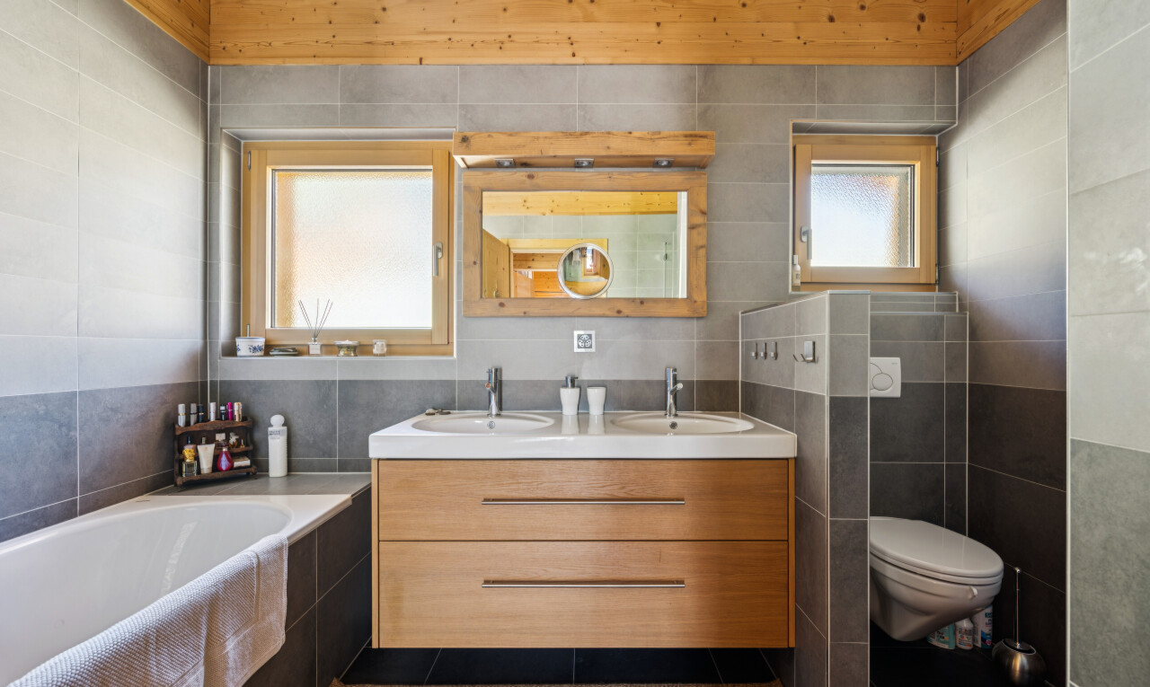 full bath with tile walls, double vanity, a garden tub, and dark tile patterned floors