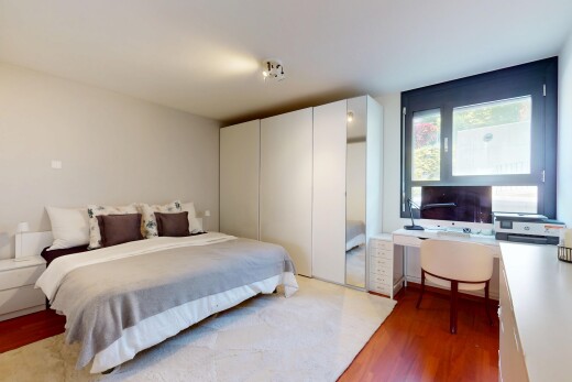 zimmer / schlafzimmer mit bürobereich, fernseher, gipskartonwand, natürliches licht, und holzfußboden