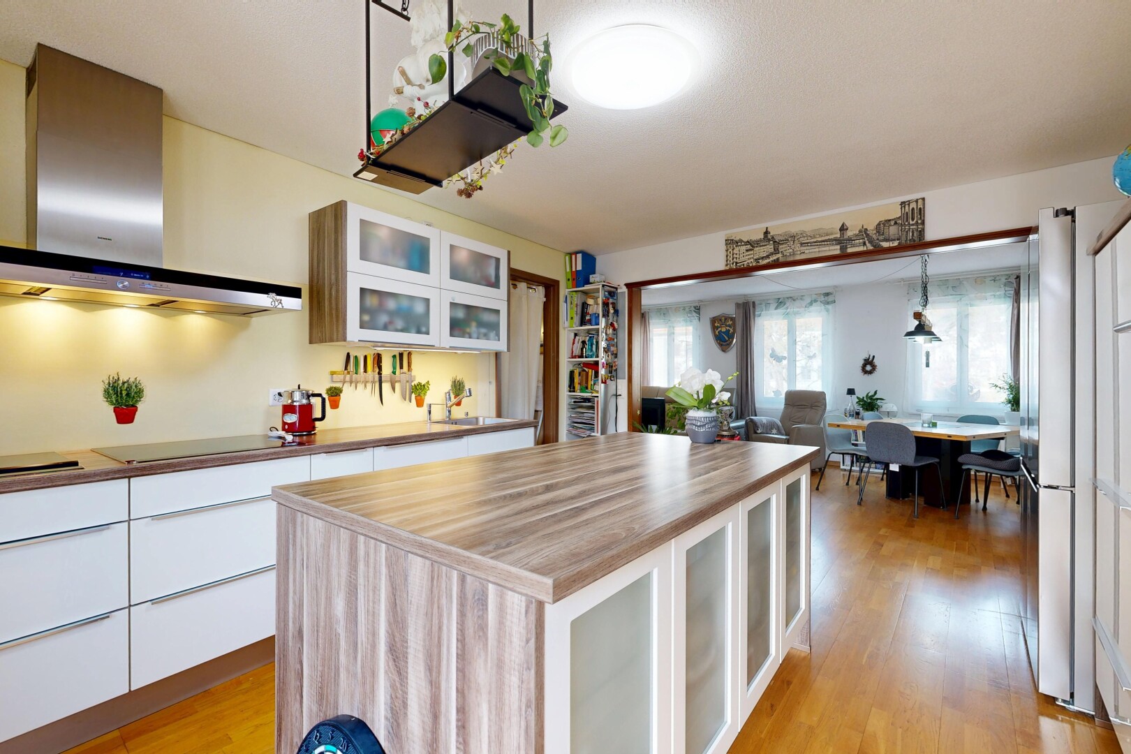 cuisine avec armoires avec insert en verre, armoires blanches, hotte, sol en finition bois, et wood finish floor