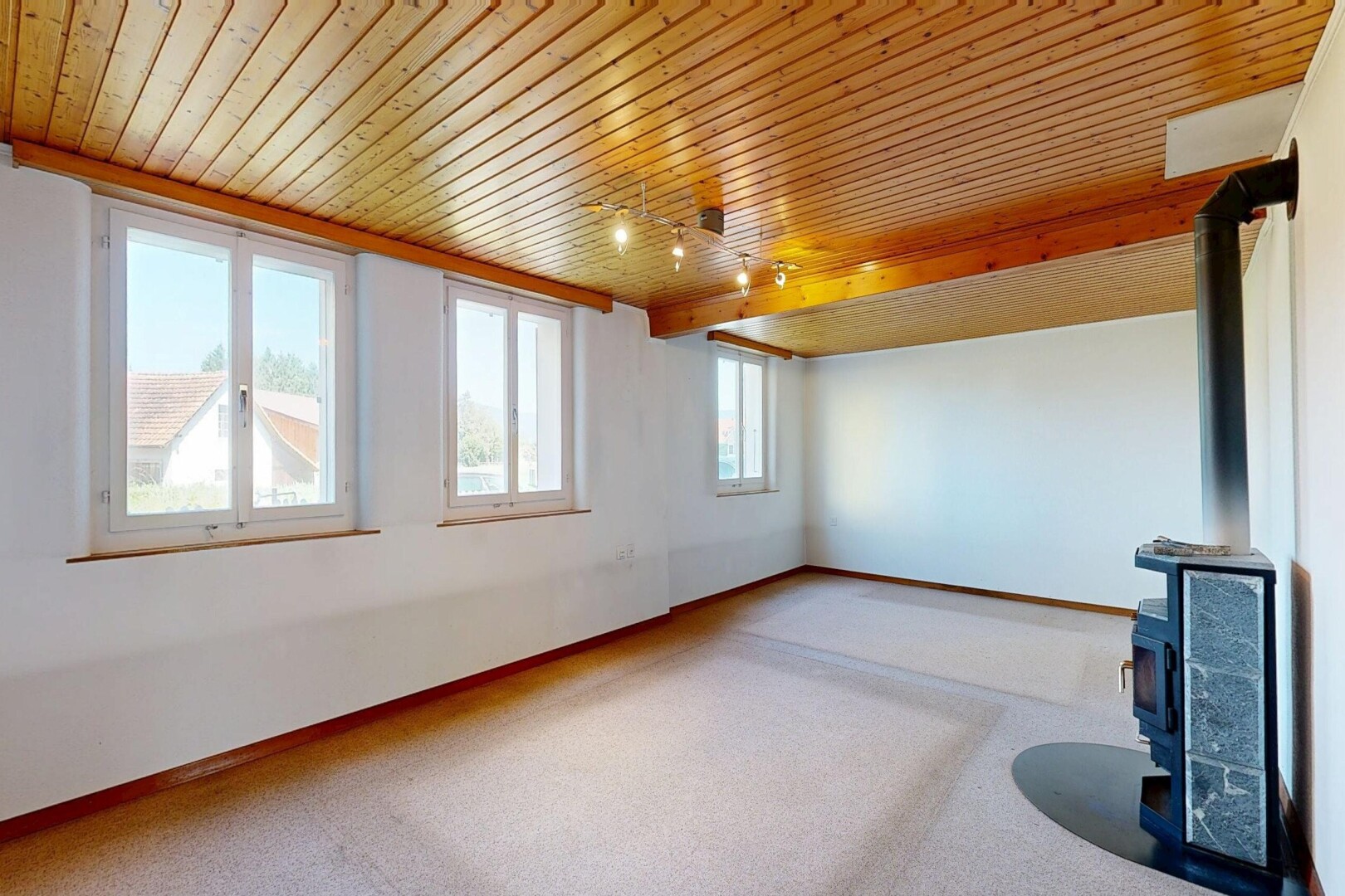 carpeted spare room featuring a wood stove and a wooden ceiling with exposed beams