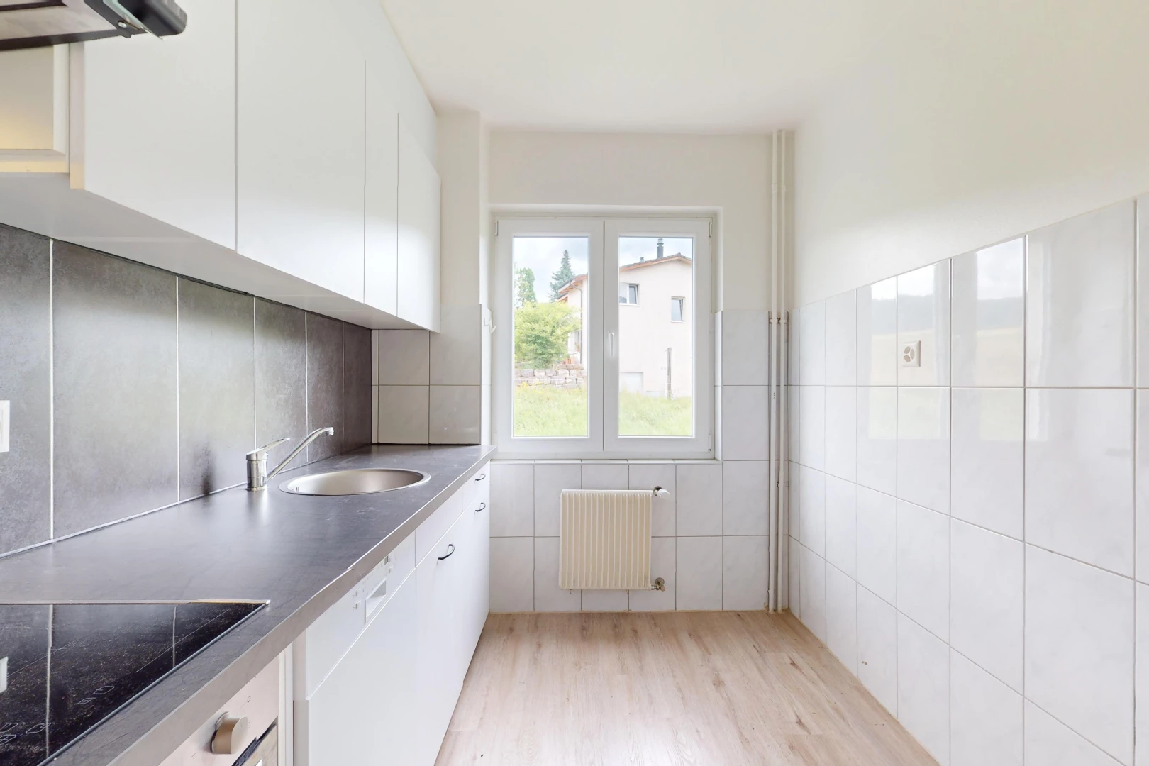 cuisine avec lumière naturelle, plancher de bois, radiateur, vasque, et mur carrelé