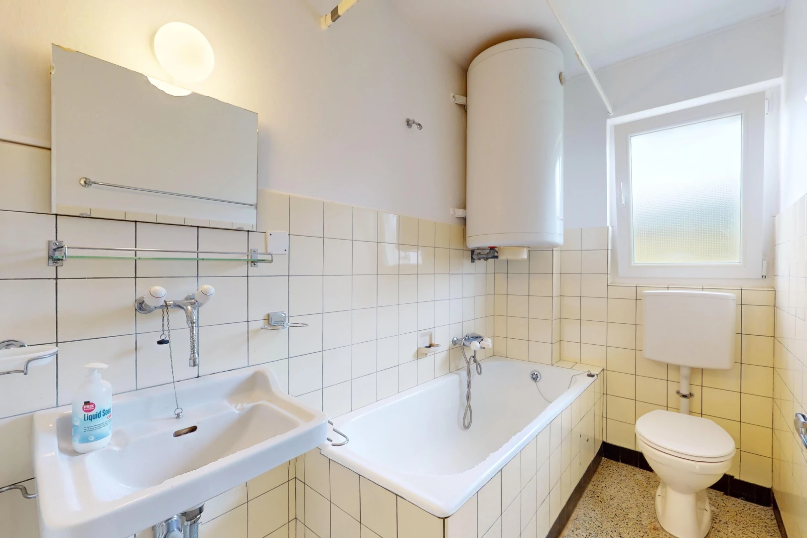 salle de bains avec lumière naturelle, miroir, sol en agrégat, toilettes, et mur carrelé