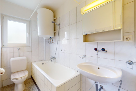 salle de bains avec chaudière, toilettes, sol en agrégat, lumière naturelle, et mur carrelé