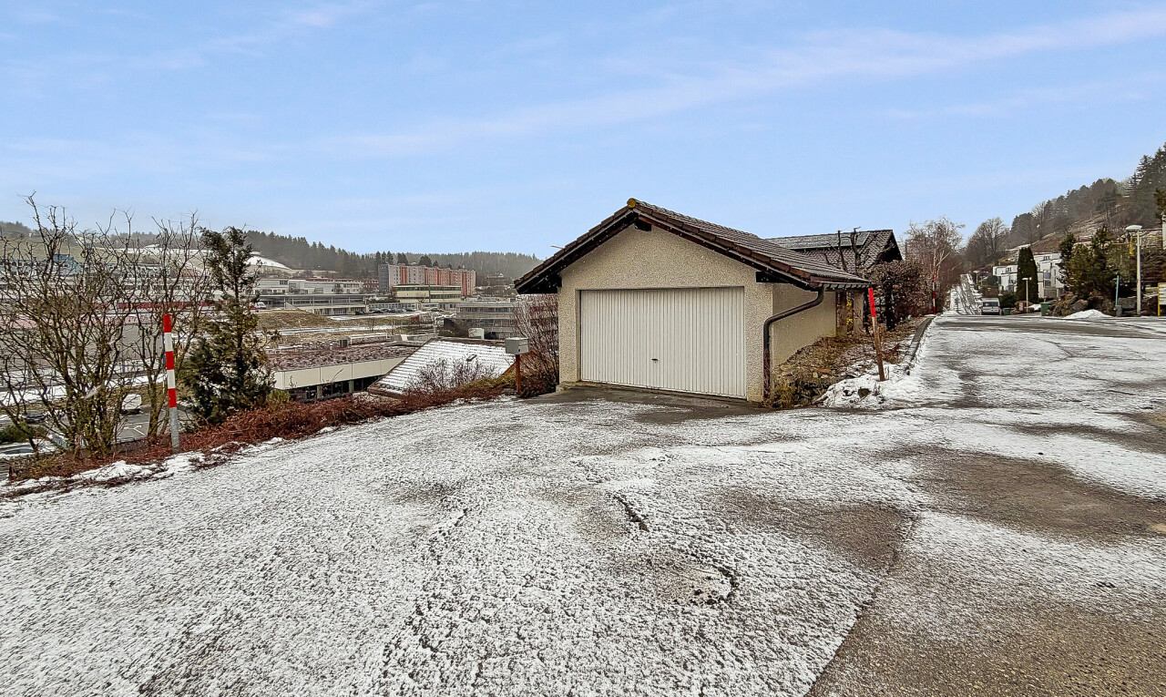 snow covered house featuring roof mounted solar panels, a garage, driveway, and stucco siding