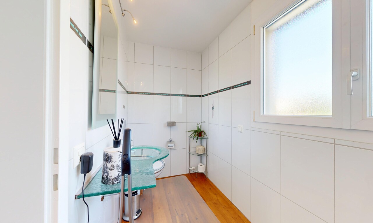 salle de bains avec mur en carrelage, tile wall, miroir, toilette, et sol en finition bois