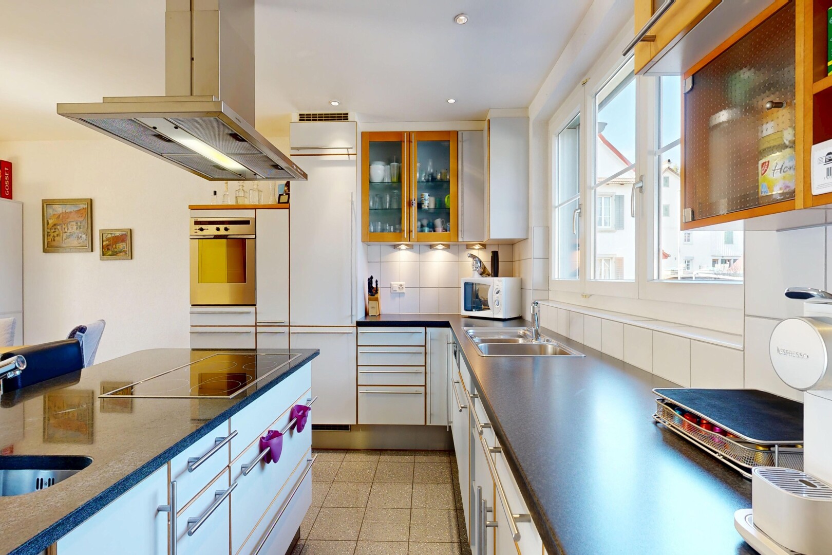 cuisine avec hotte, dark countertops, armoires avec insert en verre, glass insert cabinets, et armoires blanches