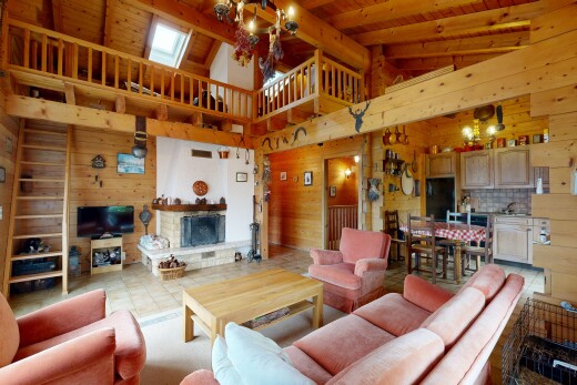 living area featuring wood walls, a fireplace with raised hearth, hanging lights, and a high wood beamed ceiling