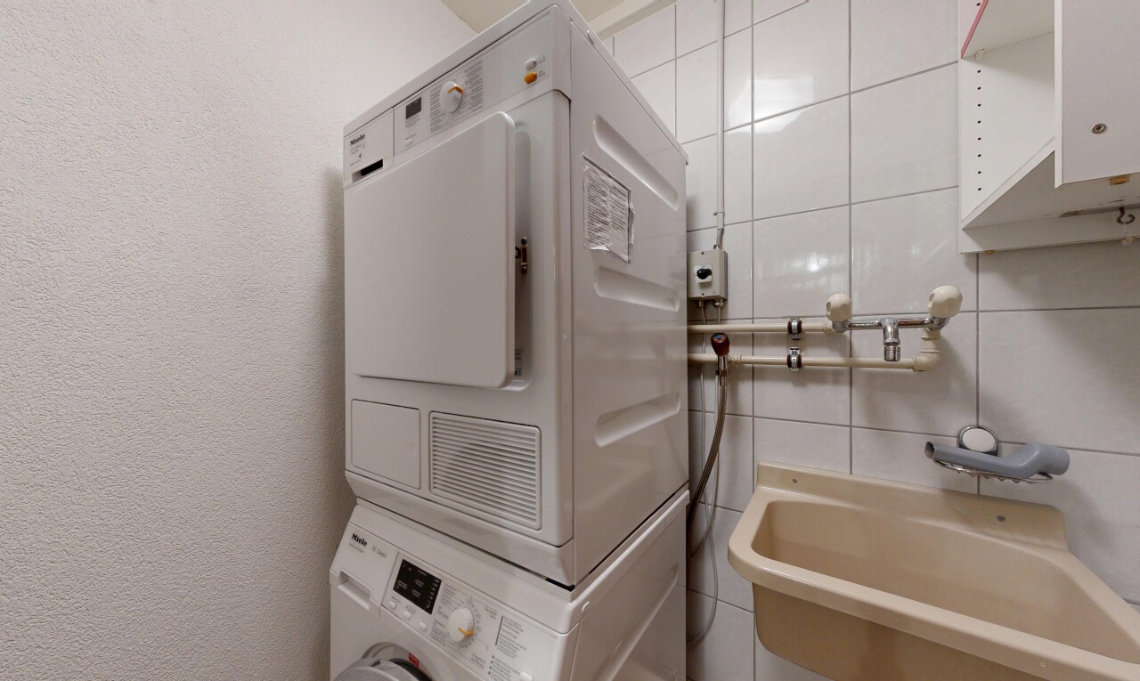 buanderie avec lave-linge et sèche-linge superposés, évier, buanderie, inside property, et mur texturé