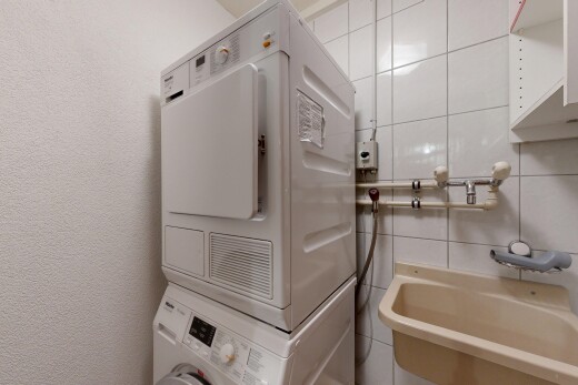 laundry area featuring stacked washer / drying machine, a textured wall, and tile walls