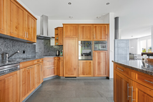 kitchen with dark stone counters, paneled dishwasher, stainless steel oven, decorative backsplash, and wood finish cabinetry