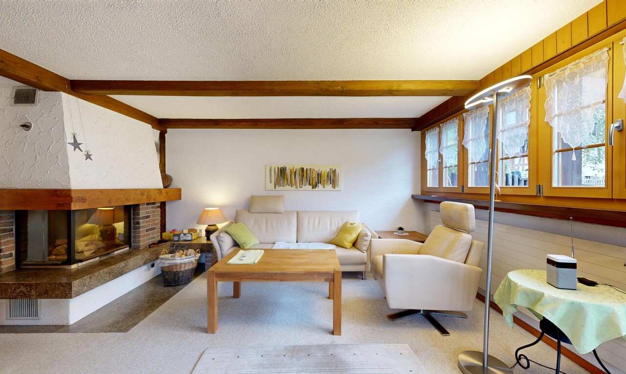 carpeted living area with a brick fireplace, beamed ceiling, and a textured ceiling