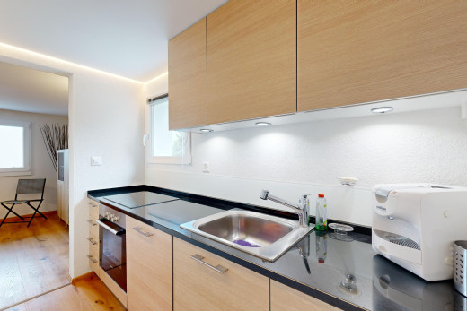cuisine avec plancher de bois, four, vasque, meubles marron clair, et lumière naturelle