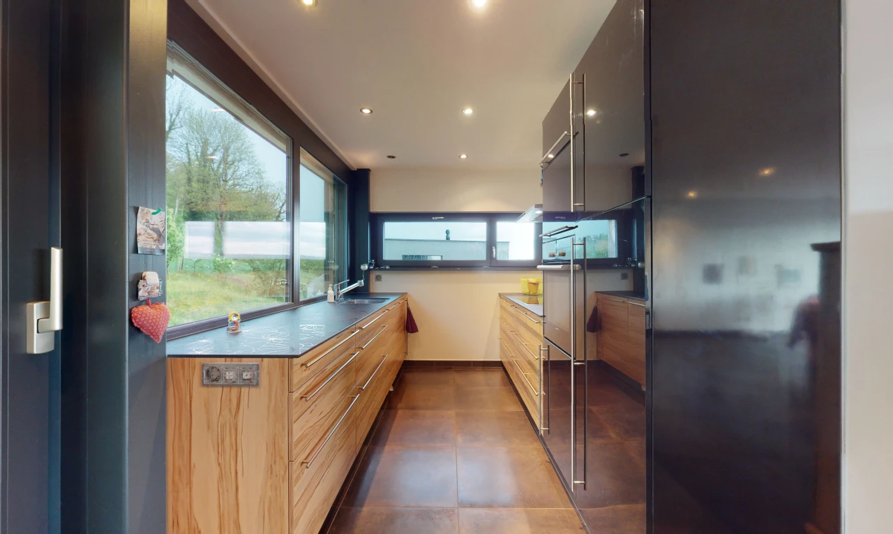 cuisine avec lumière naturelle, carrelage, sol foncé, plan de travail foncé, et meubles marron