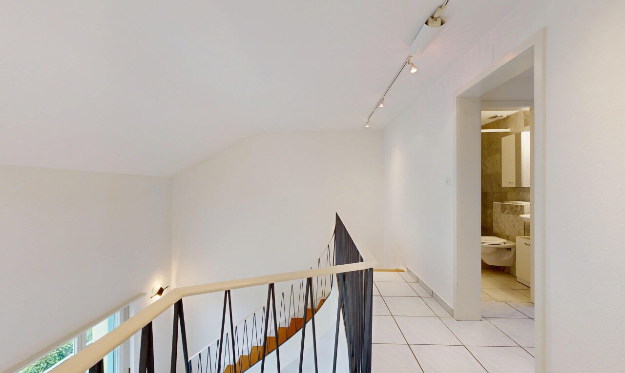 corridor featuring light tile patterned flooring, rail lighting, and an upstairs landing