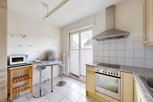 kitchen with oven, decorative backsplash, white microwave, light stone counters, and light wood finish cabinets