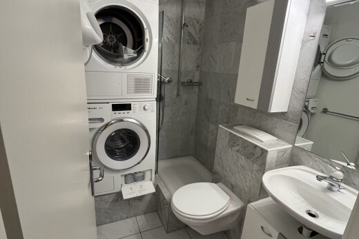 full bath featuring a marble finish shower, stacked washer / dryer, vanity, and light tile patterned floors