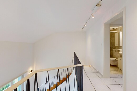 corridor featuring light tile patterned flooring, rail lighting, and an upstairs landing