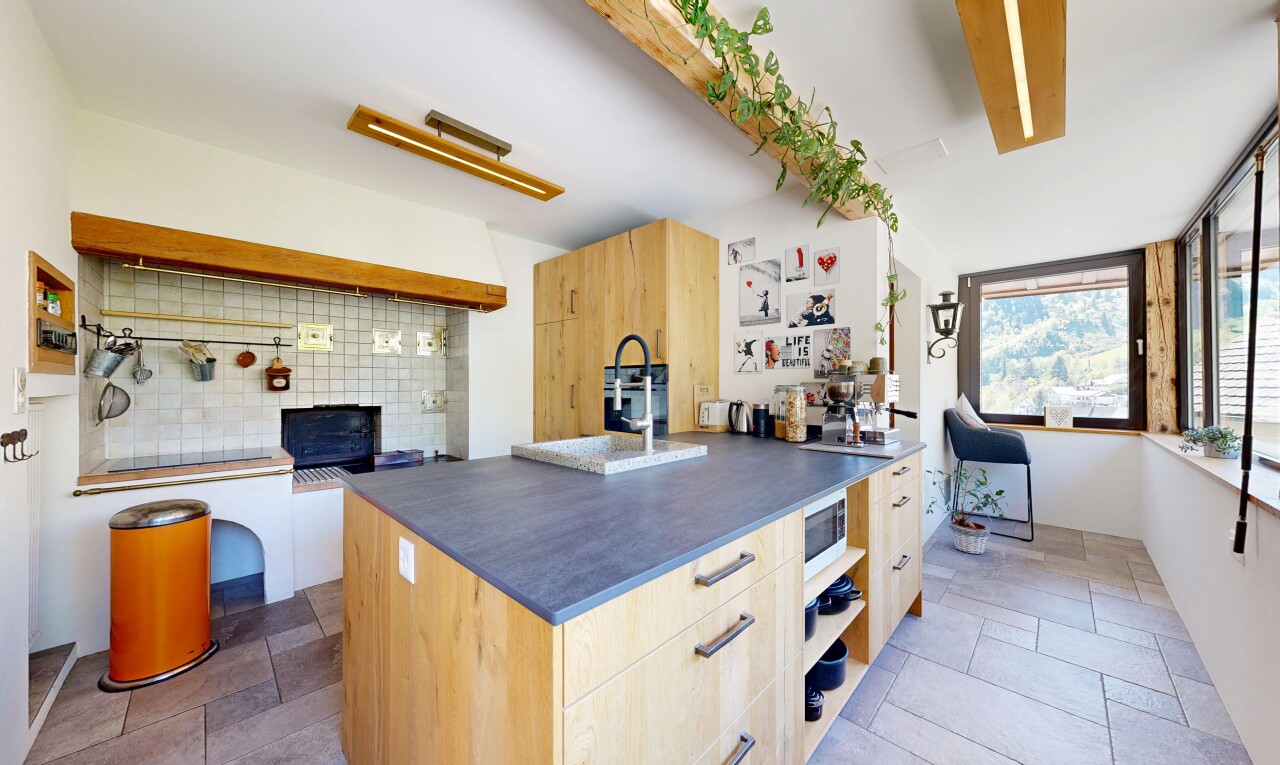 kitchen featuring light wood finish cabinetry, tasteful backsplash, stone tile flooring, a center island with sink, and white microwave