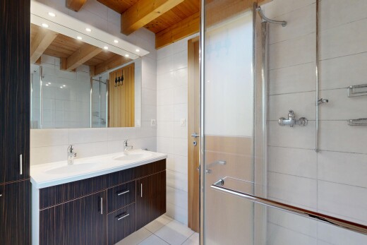 salle de bains avec mur en carrelage, tile wall, double vasque, light floor, et plafond à poutres