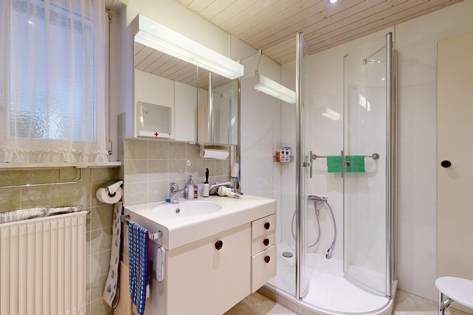 salle de bains avec lavabo (ou coiffeuse selon le contexte), radiateur, douche, miroir, et salle de bain complète