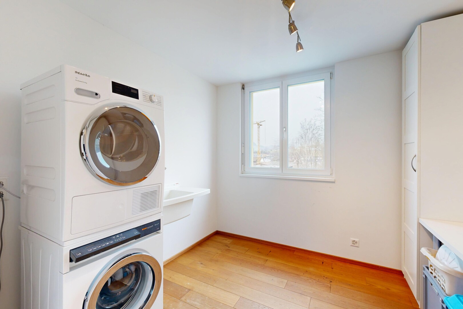 buanderie avec cloison sèche, lave-linge et sèche-linge superposés, buanderie, sol en finition bois, et lumière naturelle