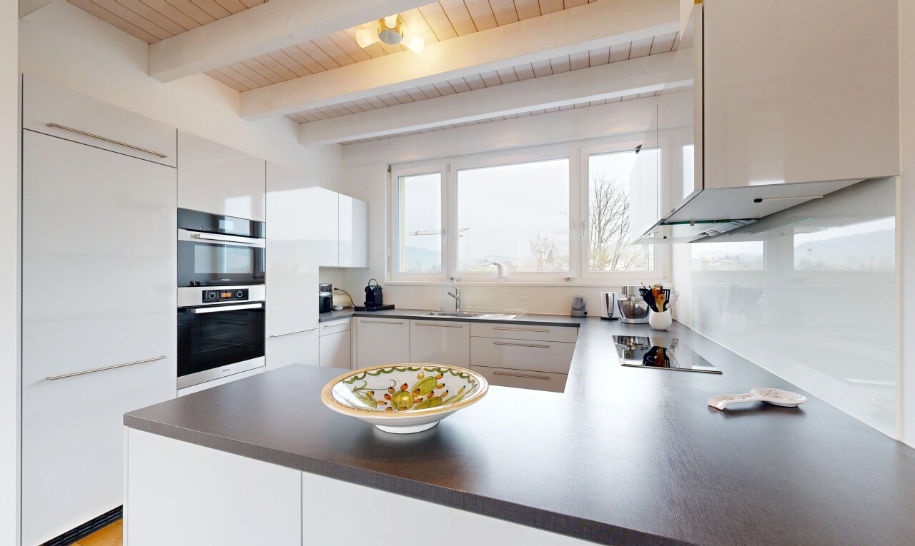cuisine avec plaque de cuisson, hotte, plafond à poutres, armoires blanches, et lumière naturelle