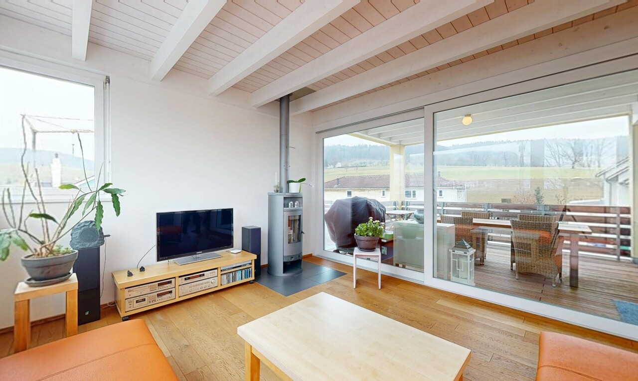 salon avec plafond à poutres, télévision, sol en finition bois, et lumière naturelle