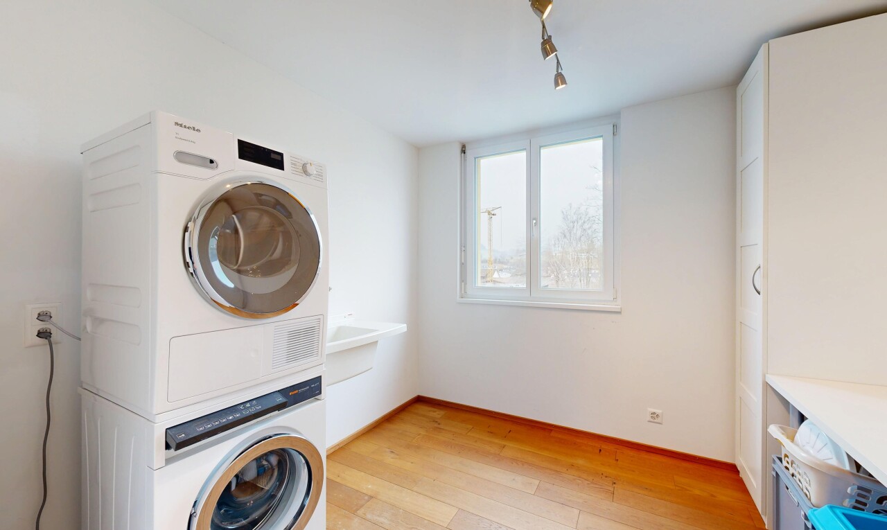 buanderie avec cloison sèche, lave-linge et sèche-linge superposés, buanderie, sol en finition bois, et lumière naturelle