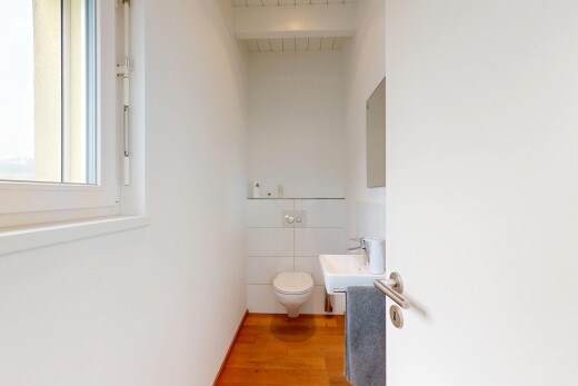 salle de bains avec lumière naturelle, miroir, sol en finition bois, et toilette