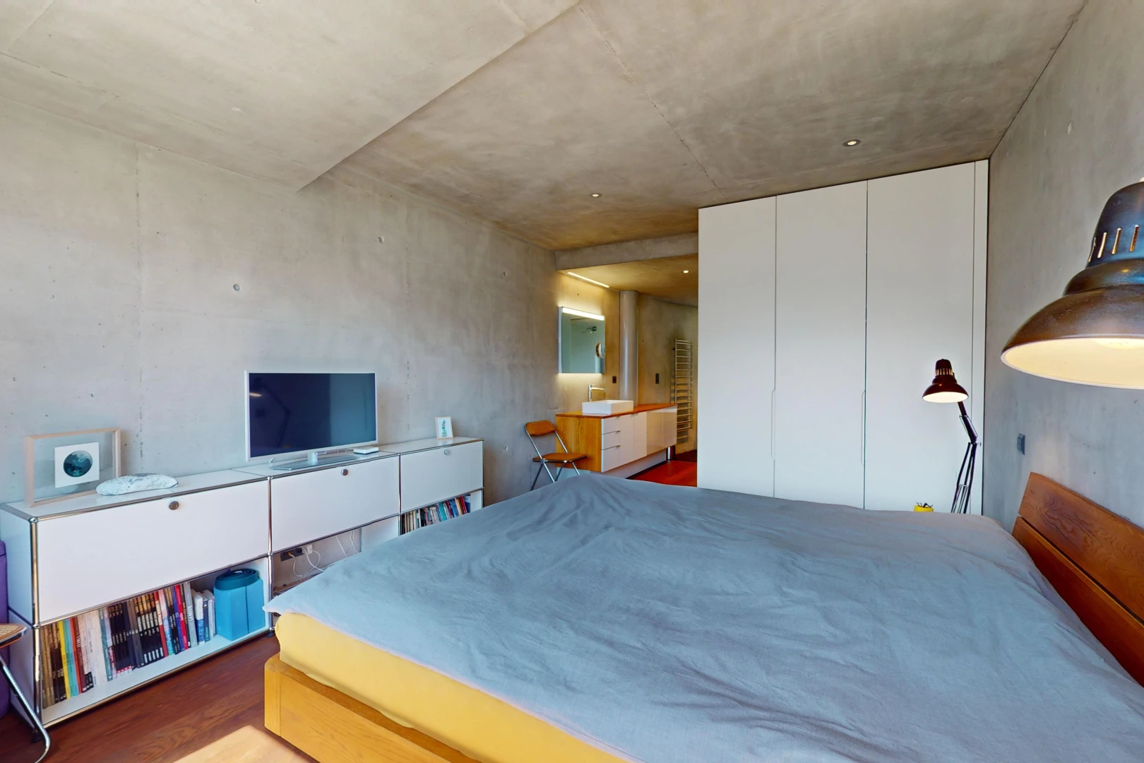 chambre avec mur en béton, plafond en béton, plancher de bois, et télévision