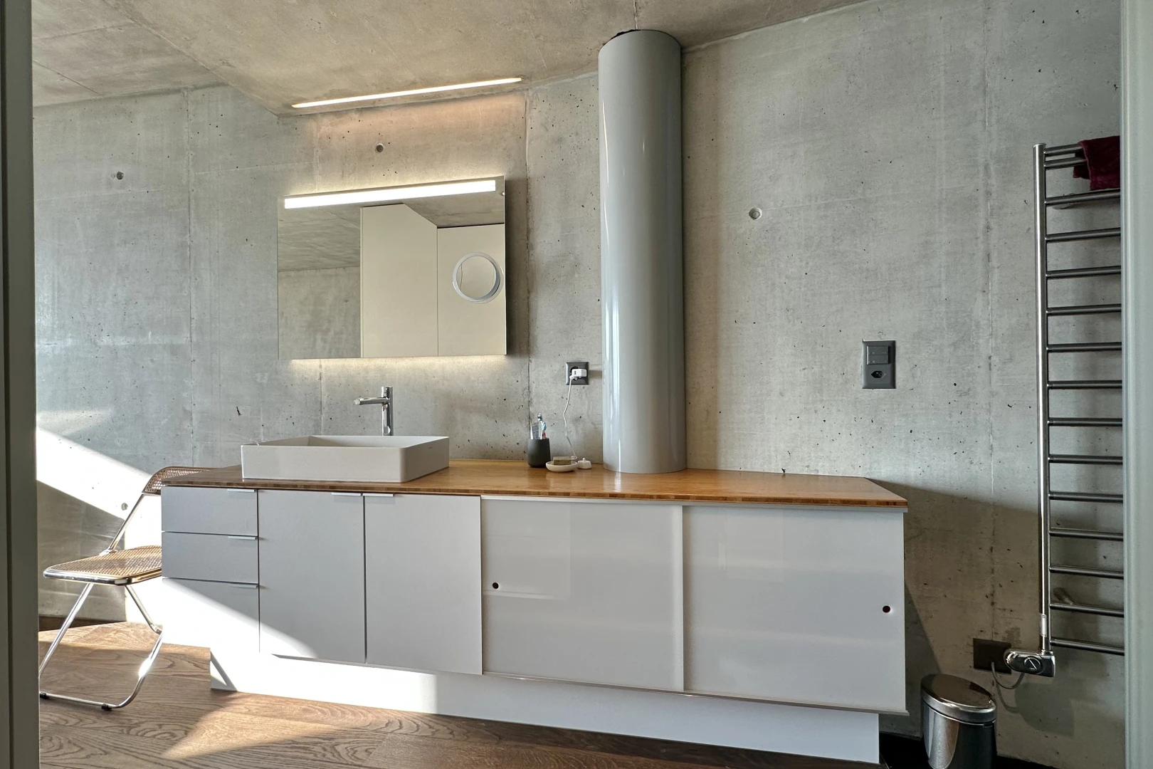 salle de bains avec mur en béton, vasque, plancher de bois, miroir, et meuble-lavabo