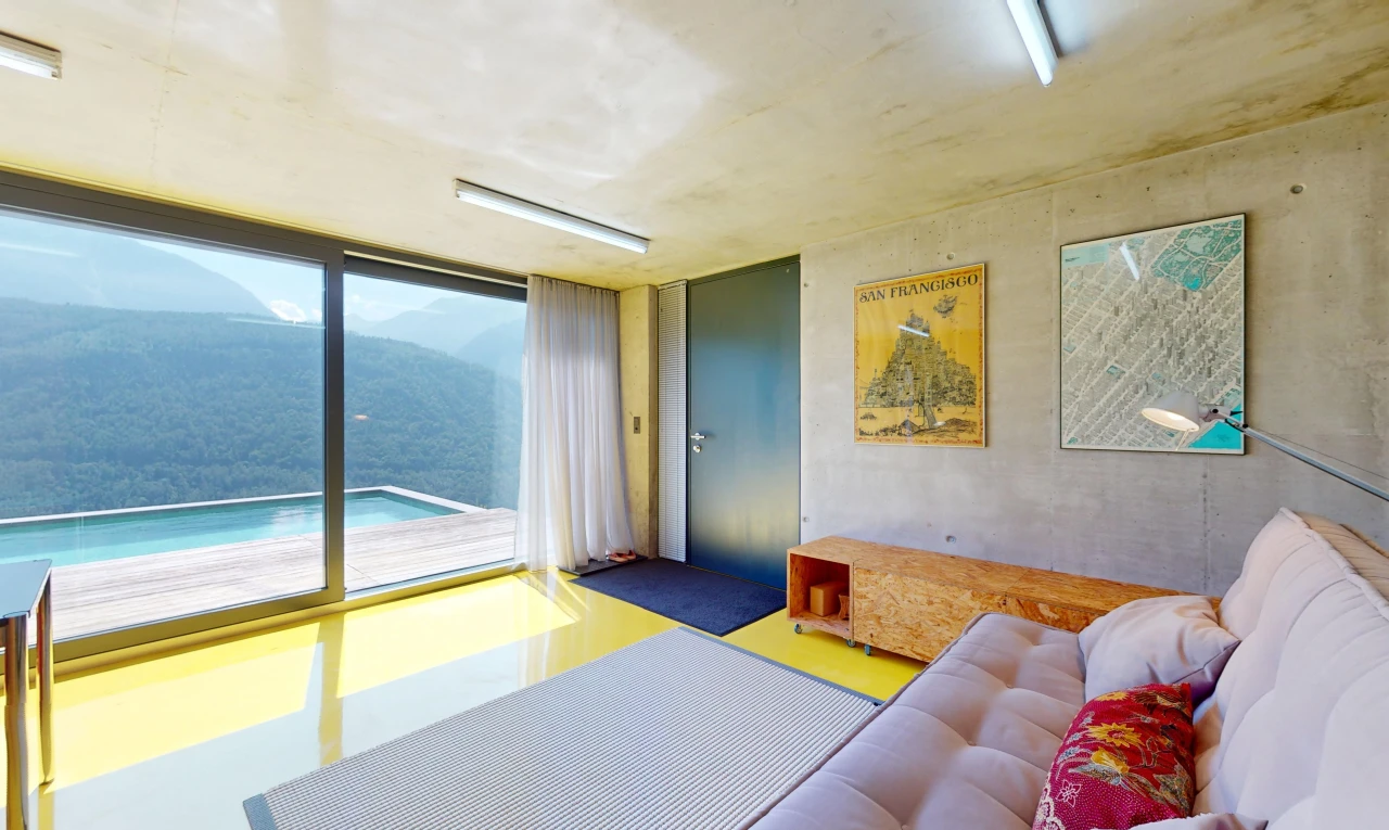 salon avec lumière naturelle, mur en béton, et vue sur la montagne