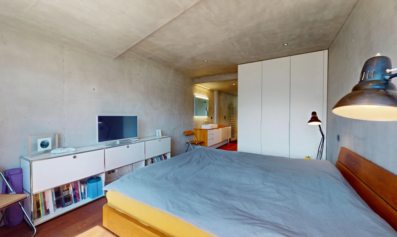 chambre avec mur en béton, plafond en béton, plancher de bois, et télévision