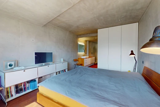 chambre avec mur en béton, plafond en béton, plancher de bois, et télévision