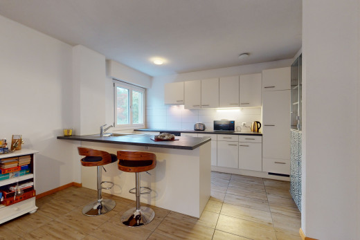 küche mit küchenrückwand, hellen fliesenböden, weissen schränken, einer mittelinsel und dunklen arbeitsplatten